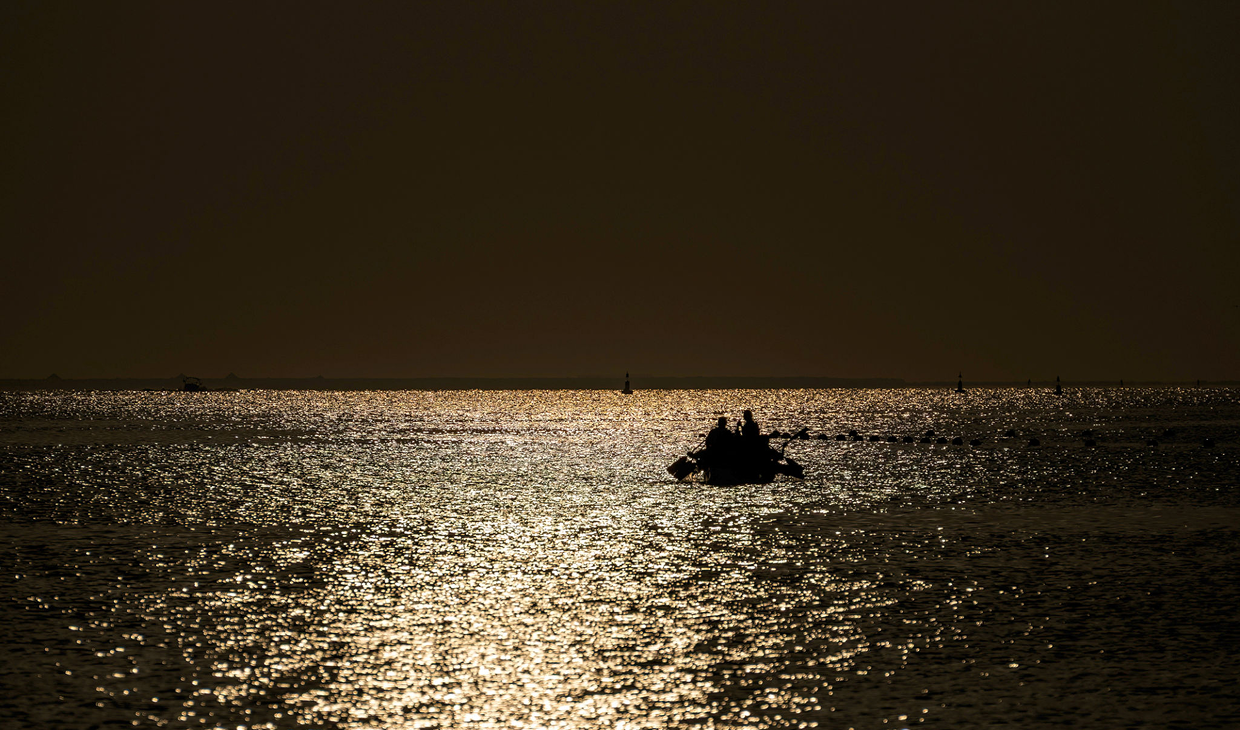 Silhouetted boat on shimmering water at dusk.