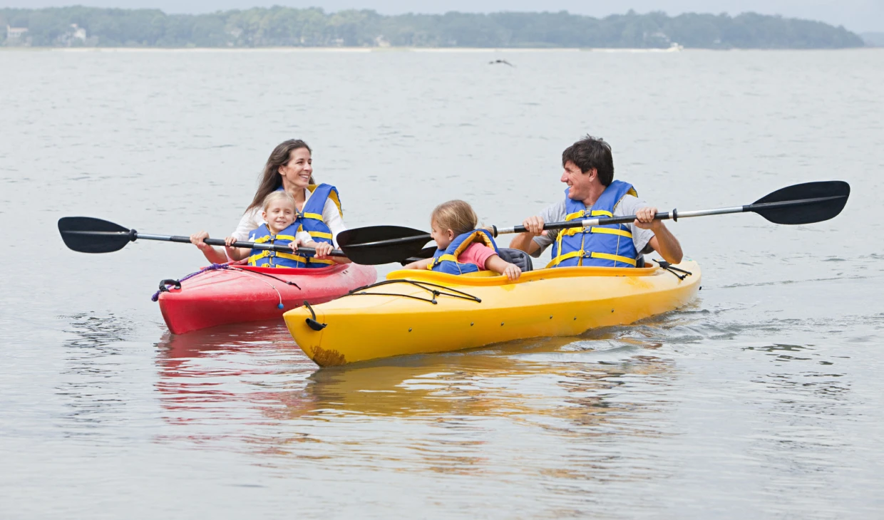 Family kayaking on calm water, wearing life vests.