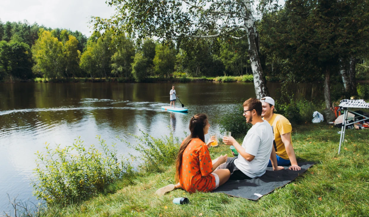 Friends relaxing by a lake, paddleboarding nearby.