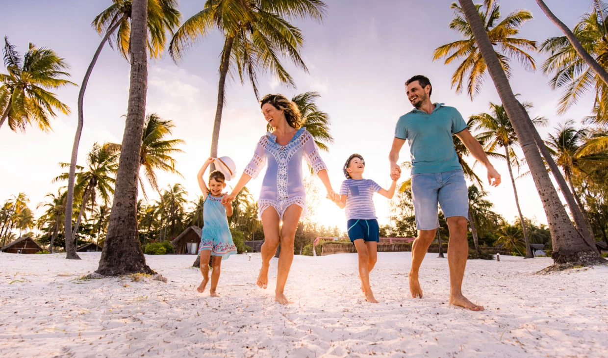 Family walking on tropical beach, holding hands.