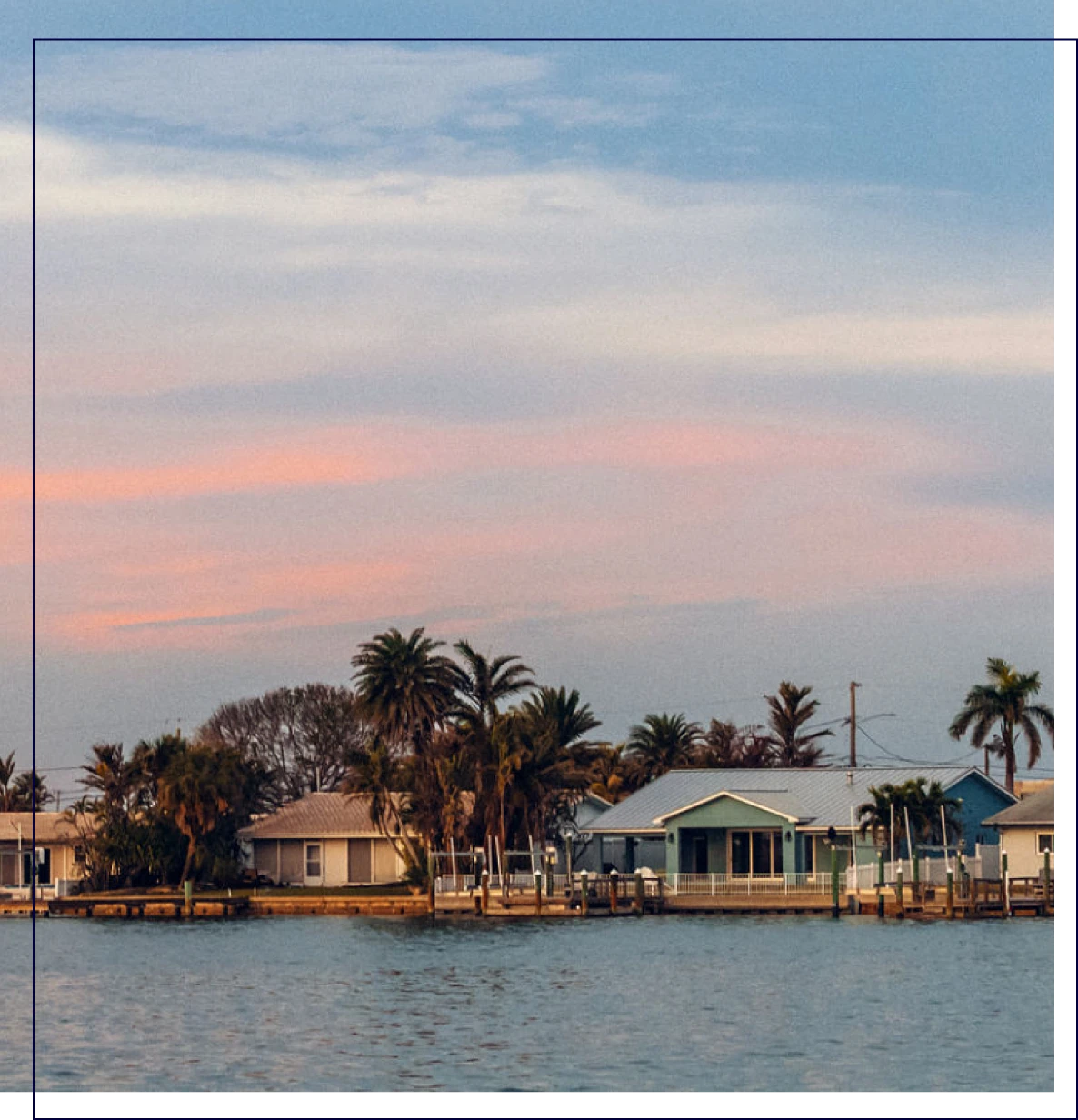 Waterfront houses with palm trees at sunset.